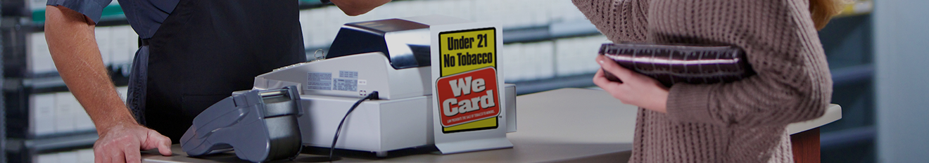 Close up of a cash register in a retail store showing the Under 21 no Tobacco We Card sign in yellow, red and white