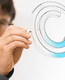 Partial image of a man wearing glasses and a long-sleeved dark shirt, showing mostly his hand drawing a copyright symbol on a transparent wall.