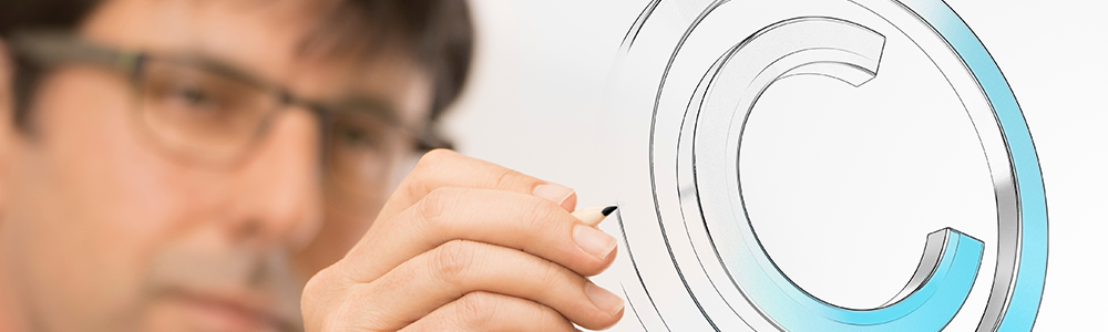 Partial image of a man wearing glasses and a long-sleeved dark shirt, showing mostly his hand drawing a copyright symbol on a transparent wall.