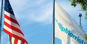 Two flag poles each with a flag raised - one with the American flag and the other with a white flag with the Philip Morris USA logo on it