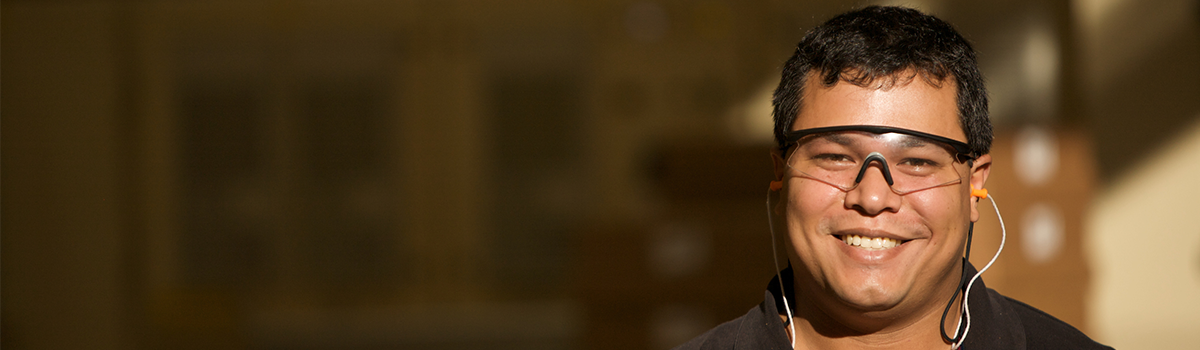 Smiling man with black framed protective lens and orange noise protectors in a black shirt