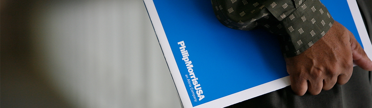 Hand sleeved in a green patterned shirt holding a royal blue and white Philip Morris USA document folder