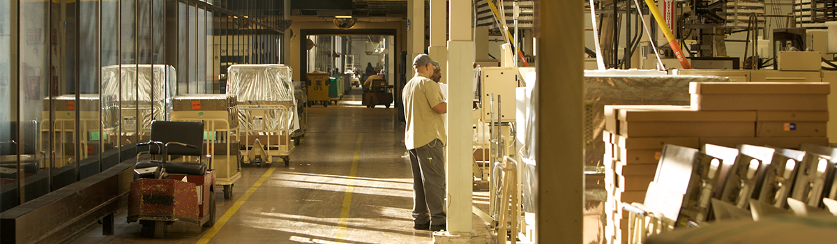 View of the walking path around the manufacturing center floor with a man in a tan t-shirt and grey pants in the mid-ground