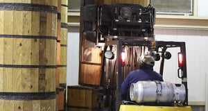 Man in blue shirt driving a forklift carrying a barrel of dried tobacco leaf