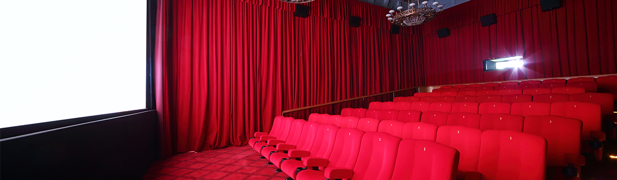 Empty movie theatre with red seats, carpet and drapes with a white viewing screen