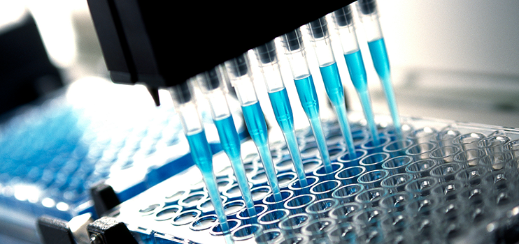 Lab machinery holding eight syringes of blue liquid over a tray of test tubes