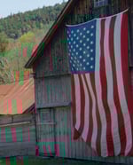 The American flag hanging roof high from the front of an old, weathered barn.