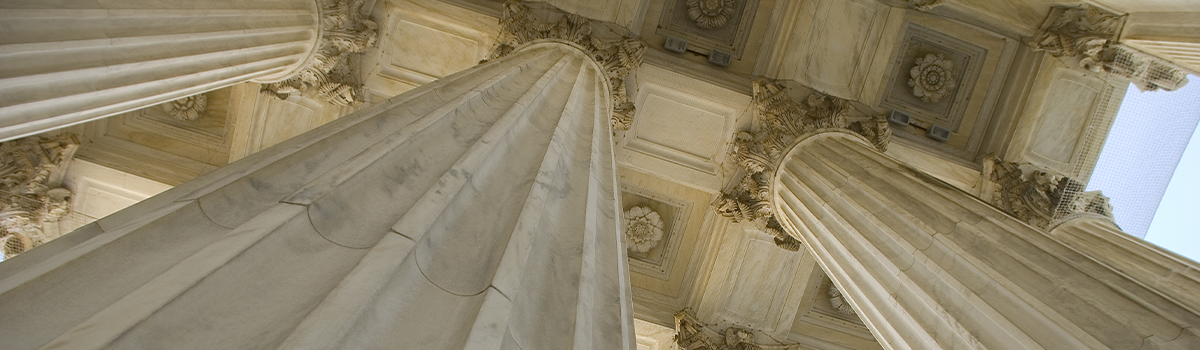 Close up of large marble columns extending to the ceiling of an ornate Greek-revival style building.