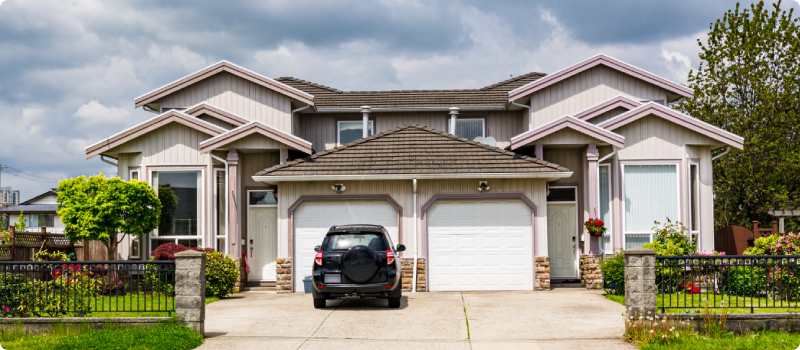 Residential duplex townhouse with black car parked on concrete driveway.