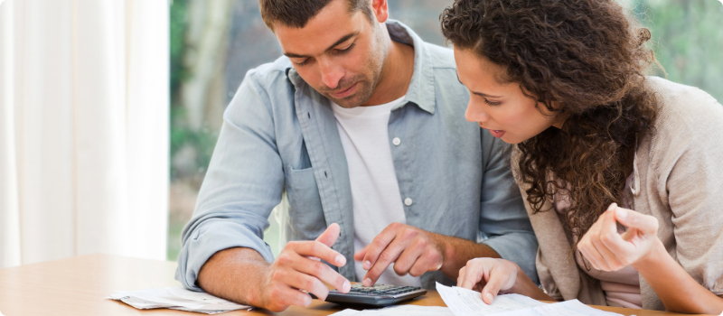A concerned couple sitting at a table, calculating their bills together.
