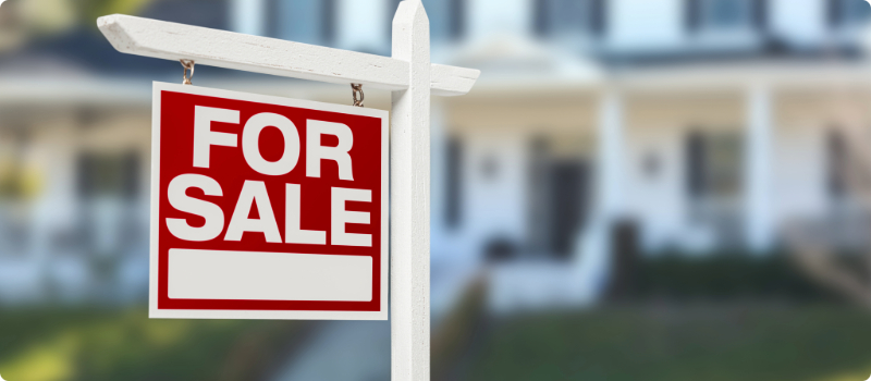 A close-up of a "For Sale" sign in a new home's yard.