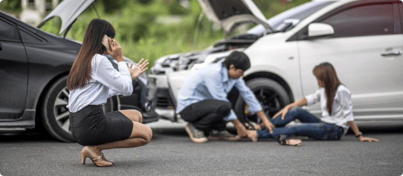 People at an auto accident scene taking care of an injured person and calling for help.
