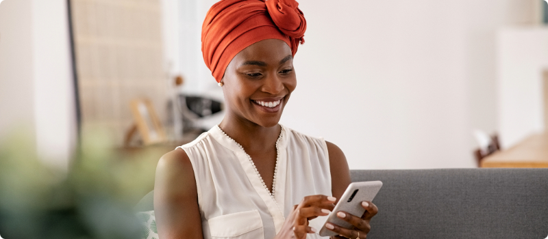 A smiling person sitting on their couch while using their phone. 
