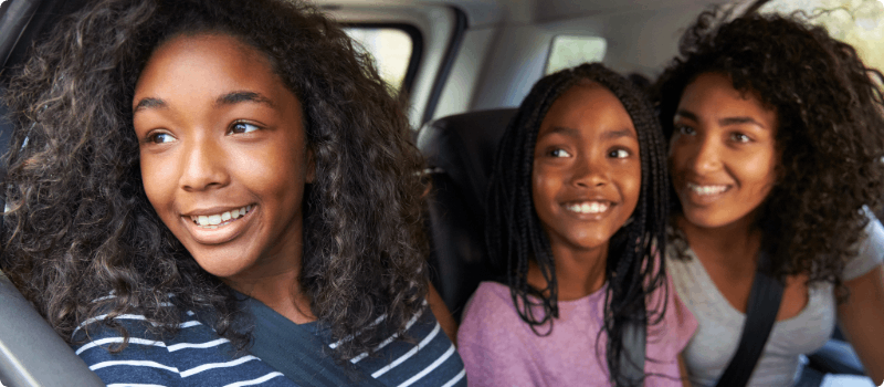 Three happy passengers looking out a vehicle's backseat window.