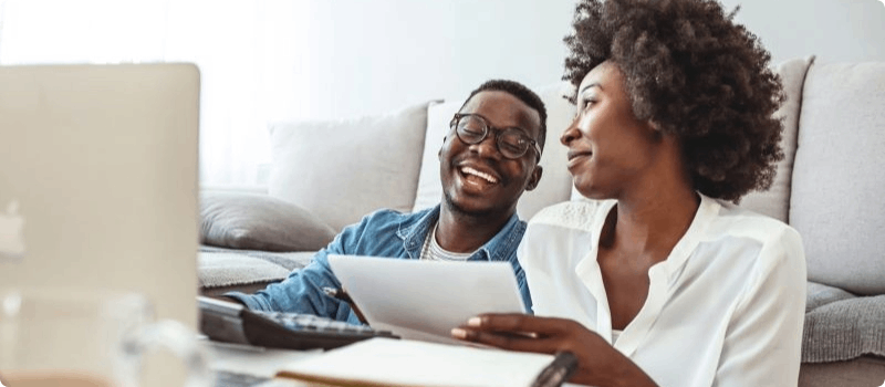 A happy couple resting on their couch while working on their laptop and phone.