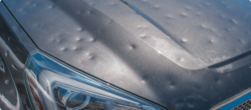The hood of a car covered in dents from a hailstorm.