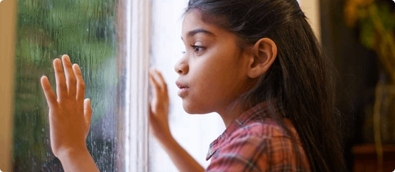 Young girl starting at a storm outside from a window.