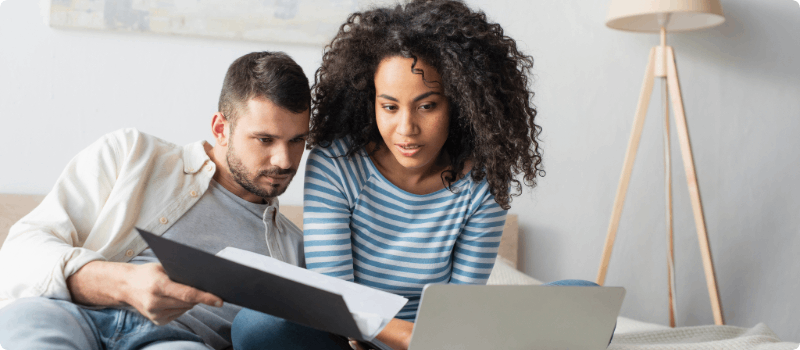 A couple looking at a laptop while holding an open folder.
