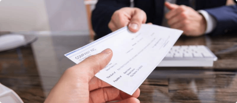 Person reaching across a desk, handing a check to another person.