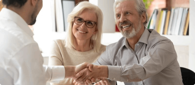 Happy couple shaking hands with a person across the desk.