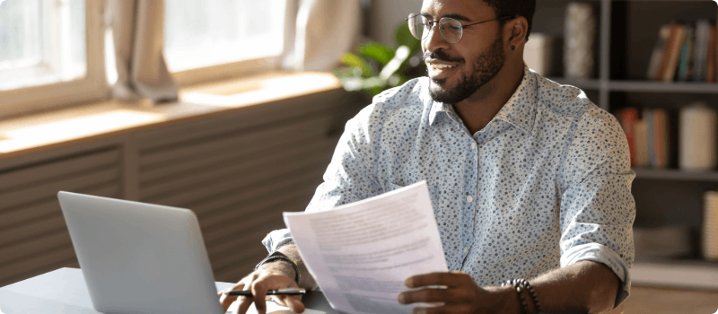 Person sitting in front of a laptop while holding a document.