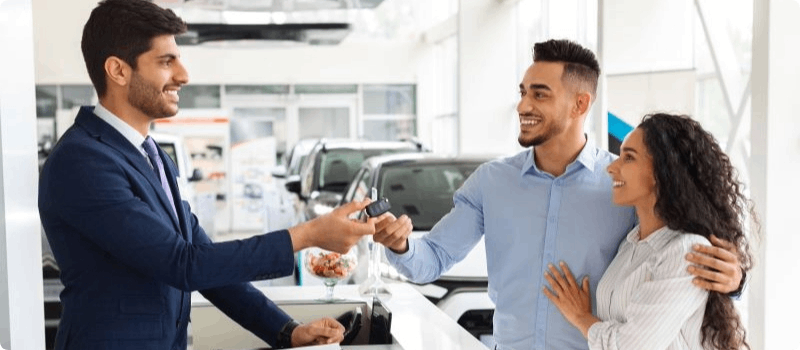 Auto salesperson handing car keys to a happy couple.