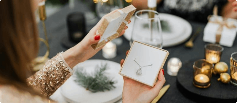 Person opening a box containing a necklace at a dinner table. 