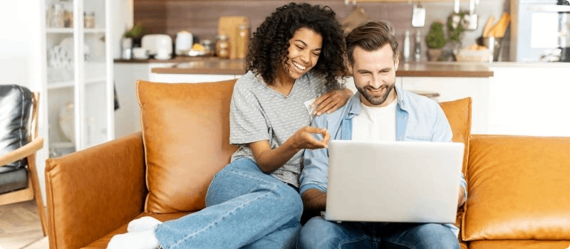 Couple sitting on a couch looking at a laptop.