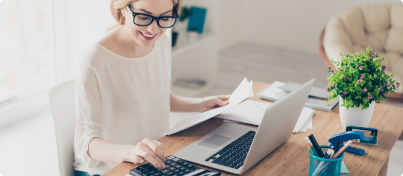 A smiling person calculating their bills at a desk.
