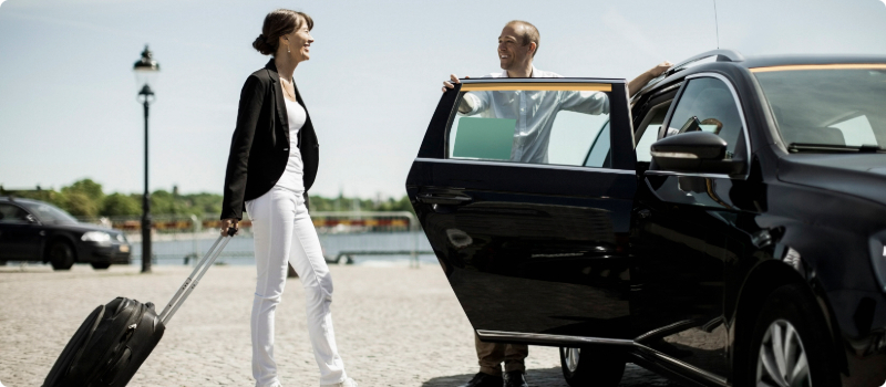 A rideshare driver holding their car door open for a passenger.