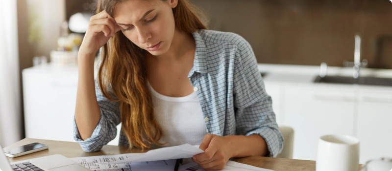 A concerned person sitting at their table while looking at a bill. 