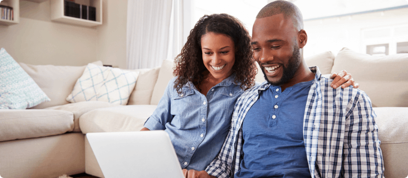 Happy couple sitting on their living room floor looking at a laptop.