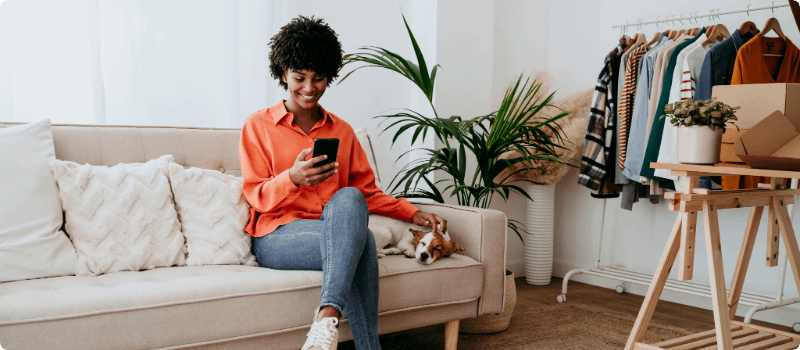 Happy person, sitting on her couch with her dog while looking at her phone.