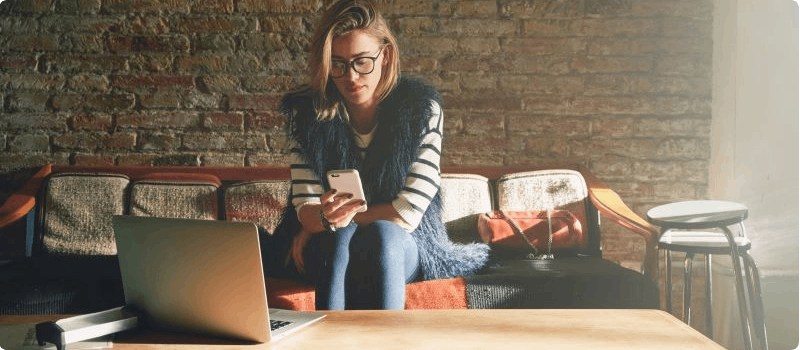 Concerned woman looking at her phone while sitting on her couch.