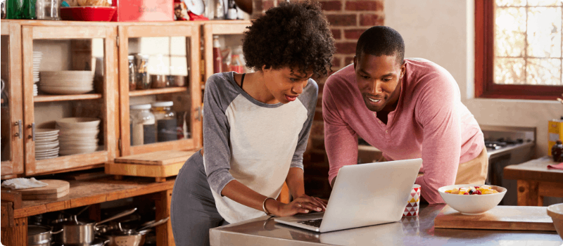Happy couple looking at a laptop in the kitchen.