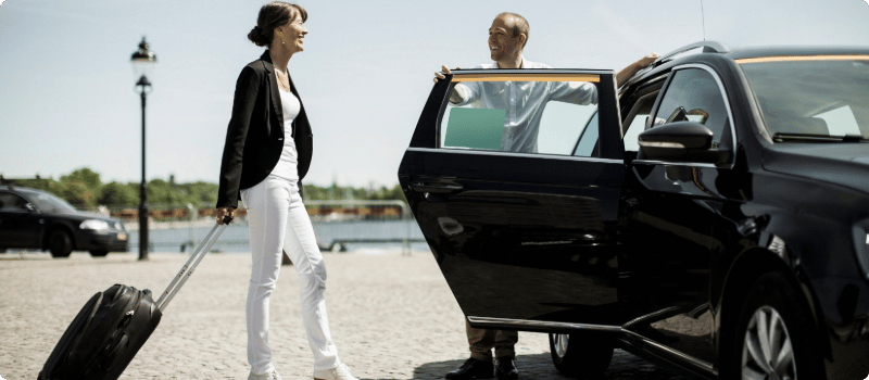 A rideshare driver holding their car door open for a passenger.