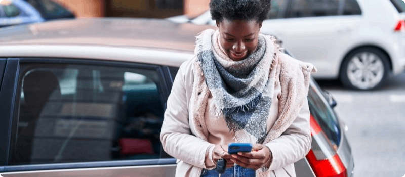 Stranded person leaning against her vehicle while looking at her phone.
