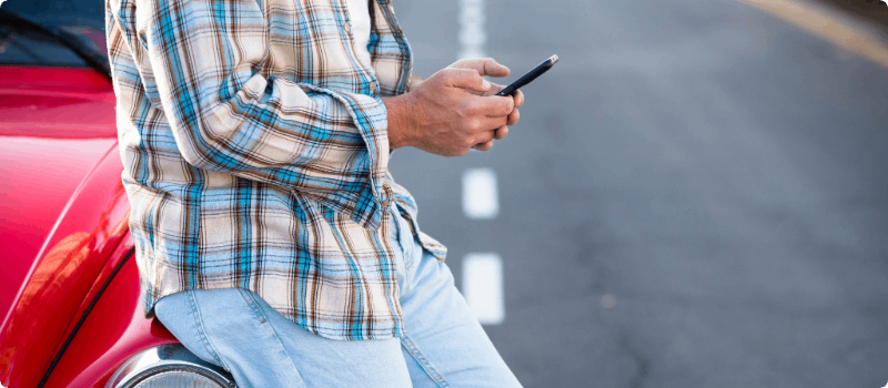 Person leaning against his broken-down vehicle while looking at his phone. 