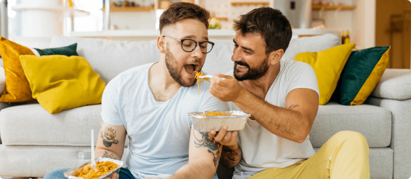 A young happy couple feeding each other in their living room.