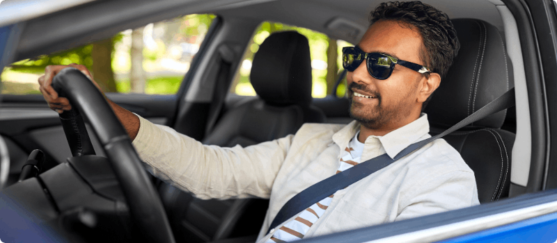 A smiling person driving on a sunny day.