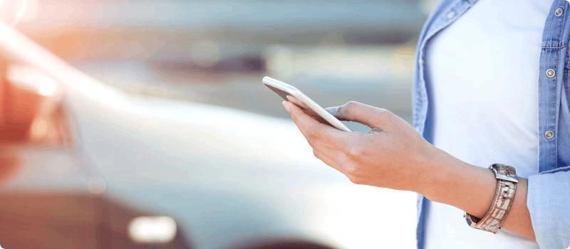Person holds their phone with their car in the background. 