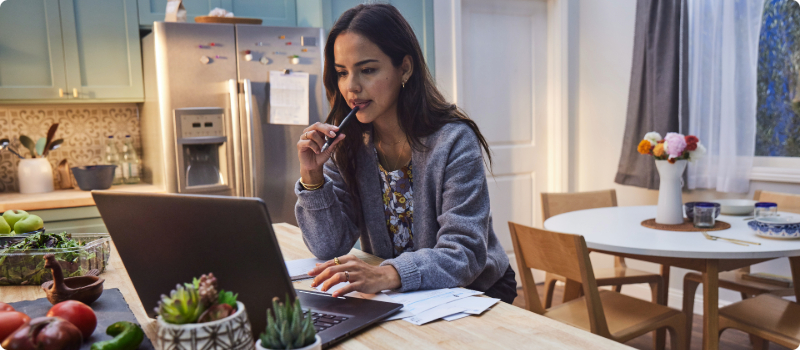 A contemplative person sitting at her kitchen counter, looking at her laptop.
