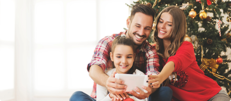 A happy family taking a selfie in front of their Christmas tree.