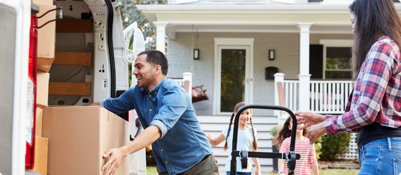 a man removing a box from a moving truck while his family watches on