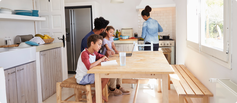 Father sitting at the dinner table with kids while mom is cooking food