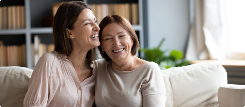 Happy senior mother and grownup daughter sitting on the couch.