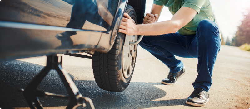 A man changing tire on the side of a road