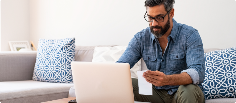 a man on his laptop and holding some paper