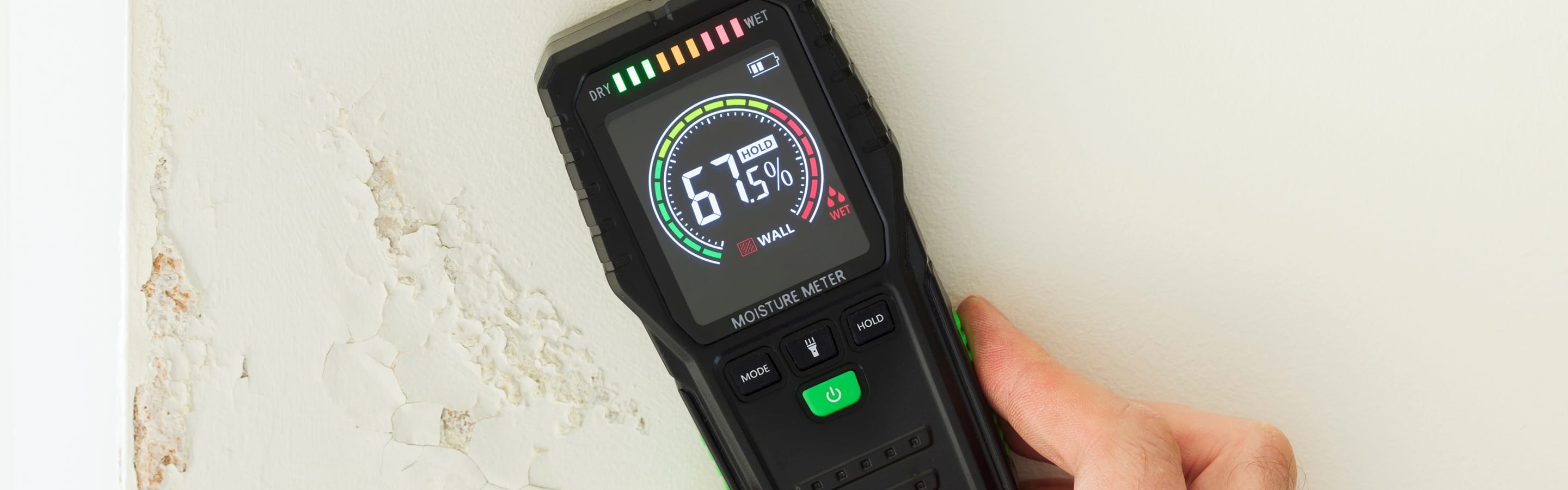 Person holding a digital humidity meter against a wall.