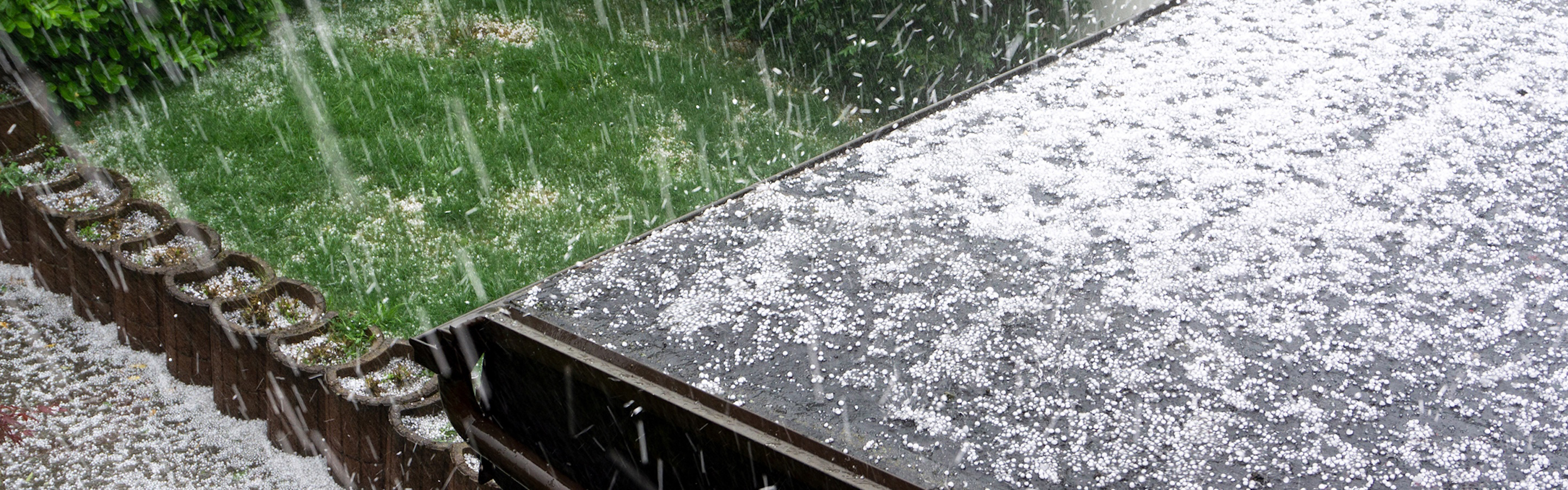 Hailstones falling in front of a house during a storm.
